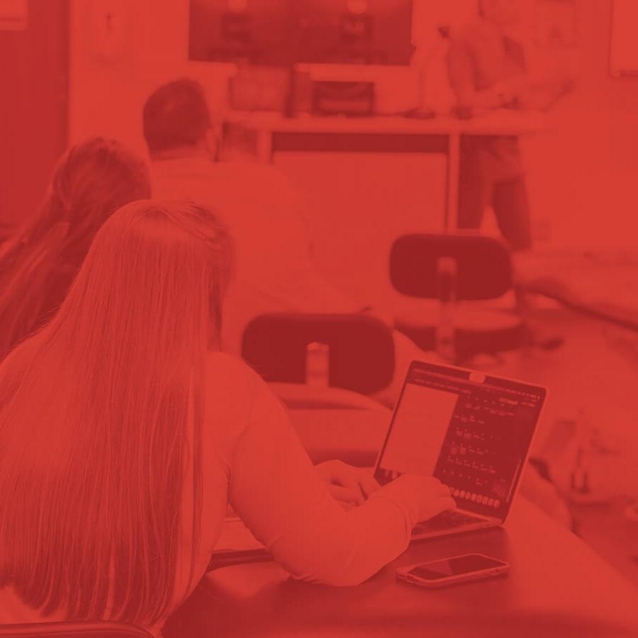 Students sitting in a classroom listening to a lecture whilst on a laptop.